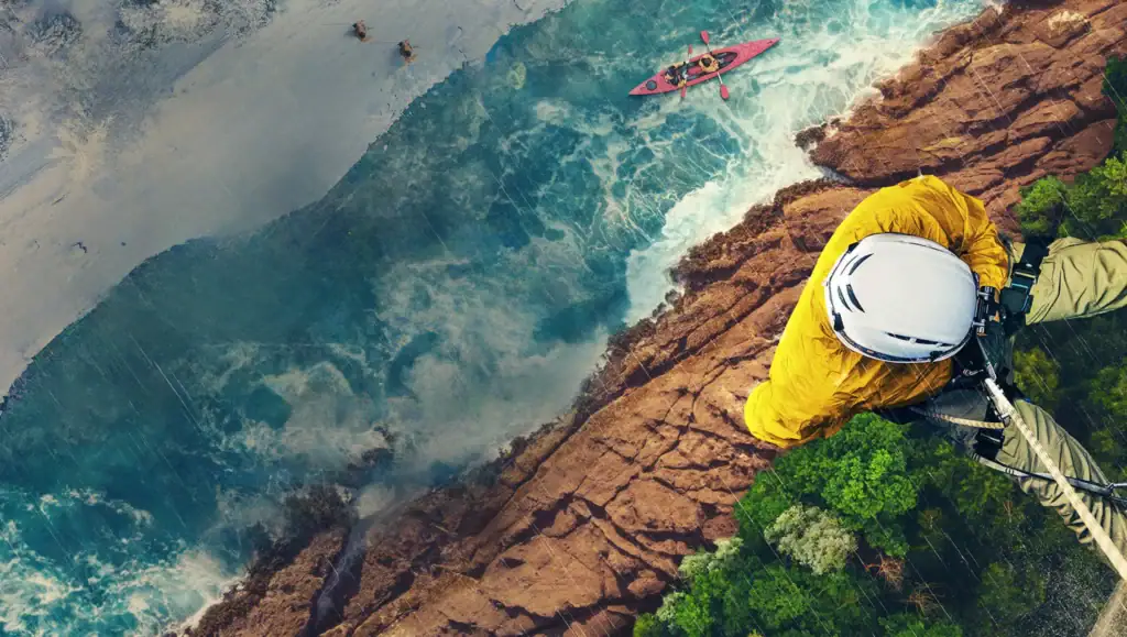 person climbing a cliff above a river